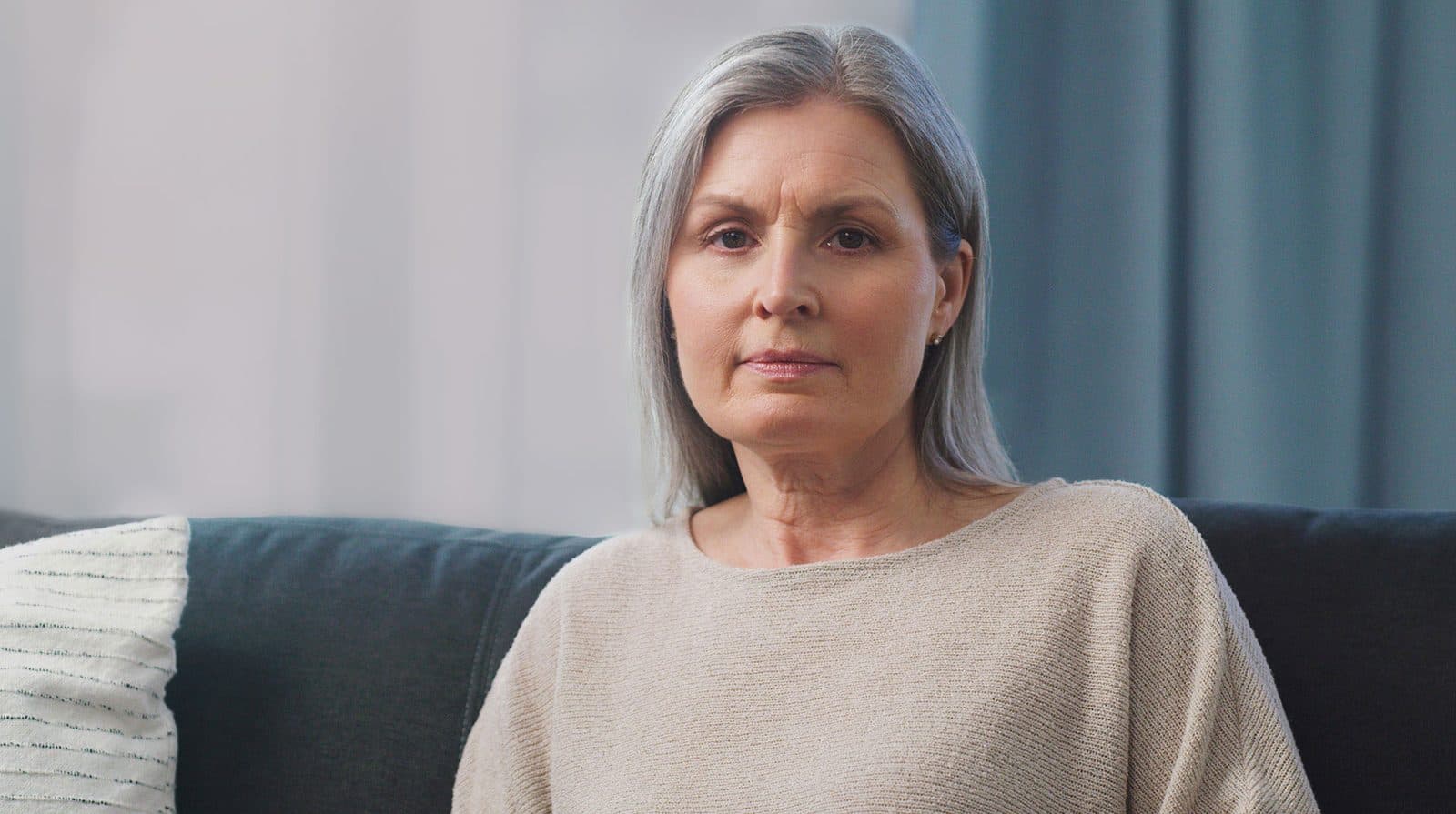 A woman in a cream sweater sitting calmly on a sofa, looking at the camera