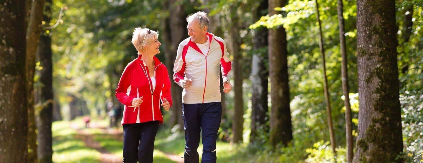 An older couple jogging along a wooded trail