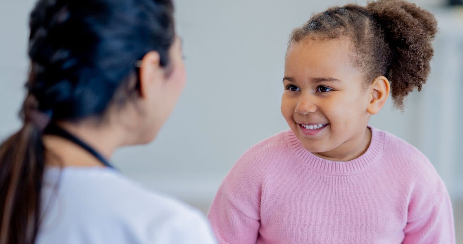A smiling girl in a pink sweater talking with her pediatrician