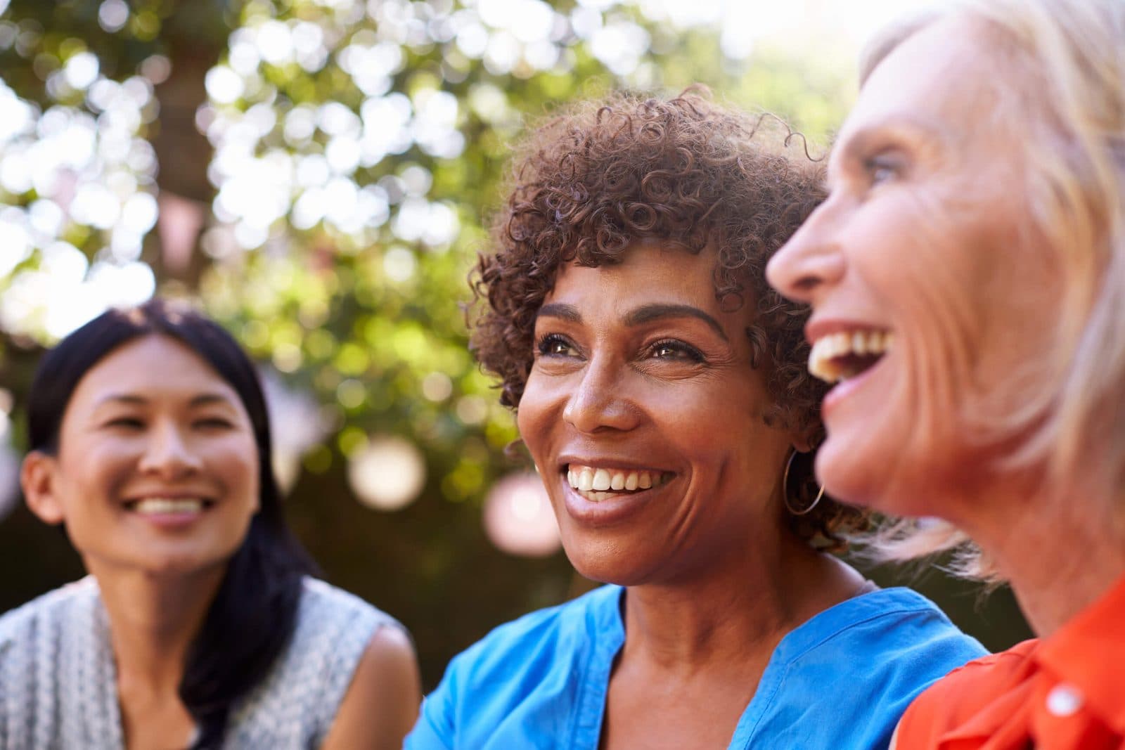 Three women of different ages laughing together outdoors