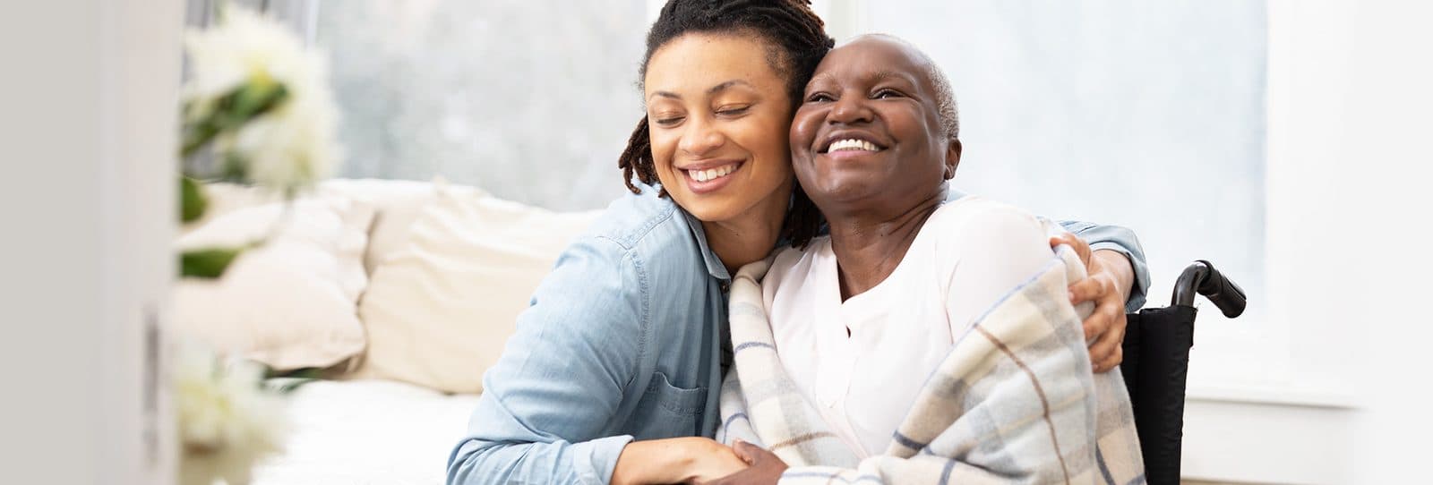 A woman hugging her smiling mother, who sits in a wheelchair